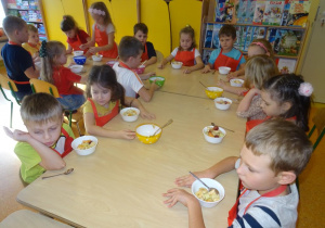 Grupa dzieci siedzi przy stole z przygotowanymi deserkami.